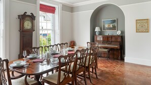 A dining room with a wooden table set for six, a grandfather clock, and a piano in the background. - Grade II Listed House in Central Exeter (Exeter)