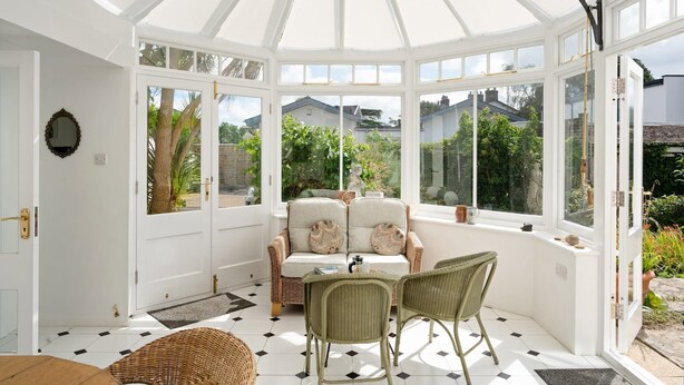 A conservatory with a white ceiling, large windows, a sofa, two chairs, and a small table. - Grade II Listed House in Central Exeter (Exeter)
