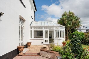A white house with a conservatory, a paved patio, and a garden with various plants. - Grade II Listed House in Central Exeter (Exeter)