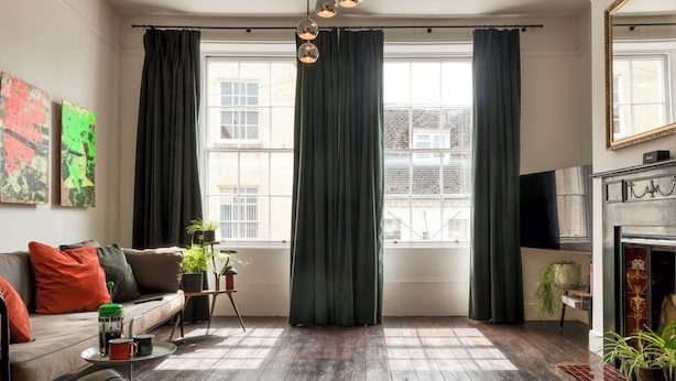 A living room with a sofa, a coffee table with a mug, a fireplace, and a large window with curtains. - The Emporium - Stylish 2BD in Winchcombe (Cheltenham)