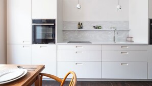 A modern kitchen with white cabinetry, a built-in oven, a marble backsplash, and pendant lighting. - The Emporium - Stylish 2BD in Winchcombe (Cheltenham)