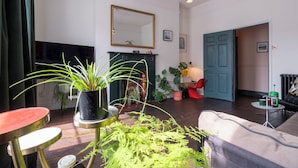 A living room with a fireplace, a large mirror, and several potted plants. - The Emporium - Stylish 2BD in Winchcombe (Cheltenham)