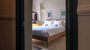 A bedroom with a wooden bed, white bedding, a small bedside table with a lamp, and two framed pictures on the wall. - The Emporium - Stylish 2BD in Winchcombe (Cheltenham)