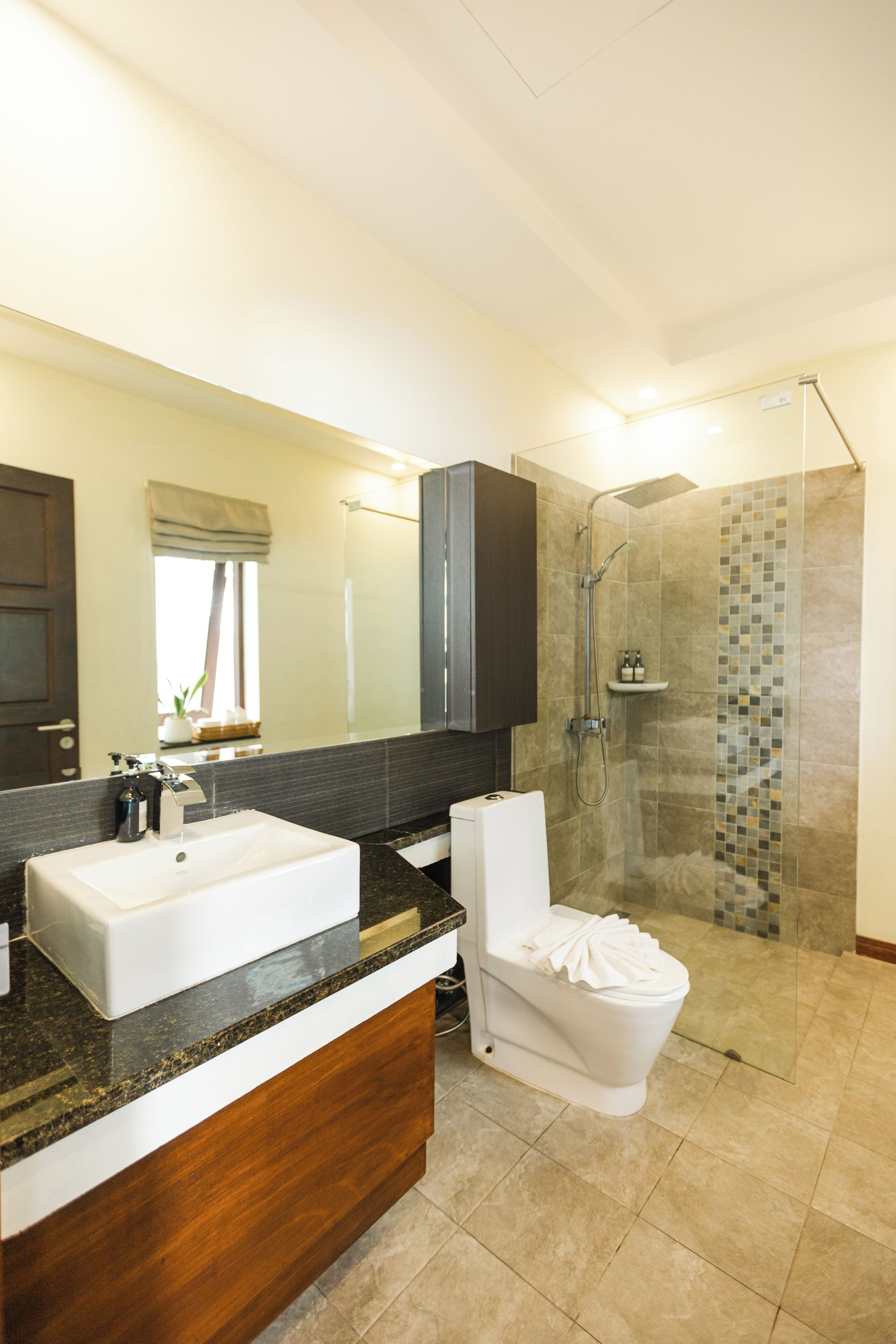 A modern bathroom with a large mirror, a white sink, a toilet, and a glass-enclosed shower area.
