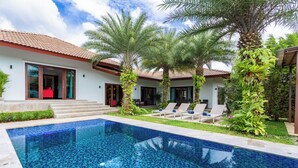 Una piscina con mosaico azul de azulejos, rodeada de palmeras y un edificio blanco con tejado de azulejos.
