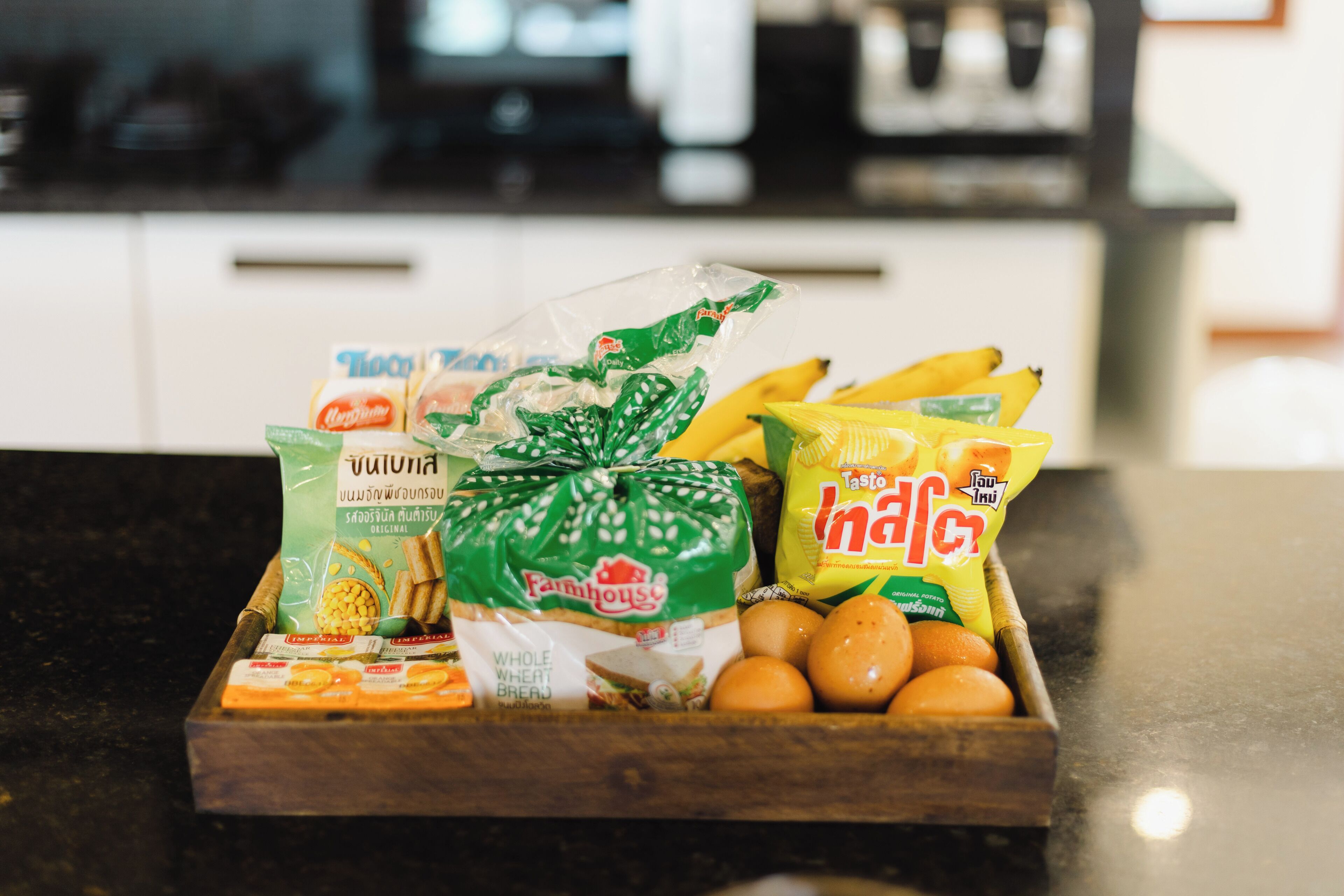 A wooden tray with various food items including whole wheat bread, eggs, bananas, and snacks.