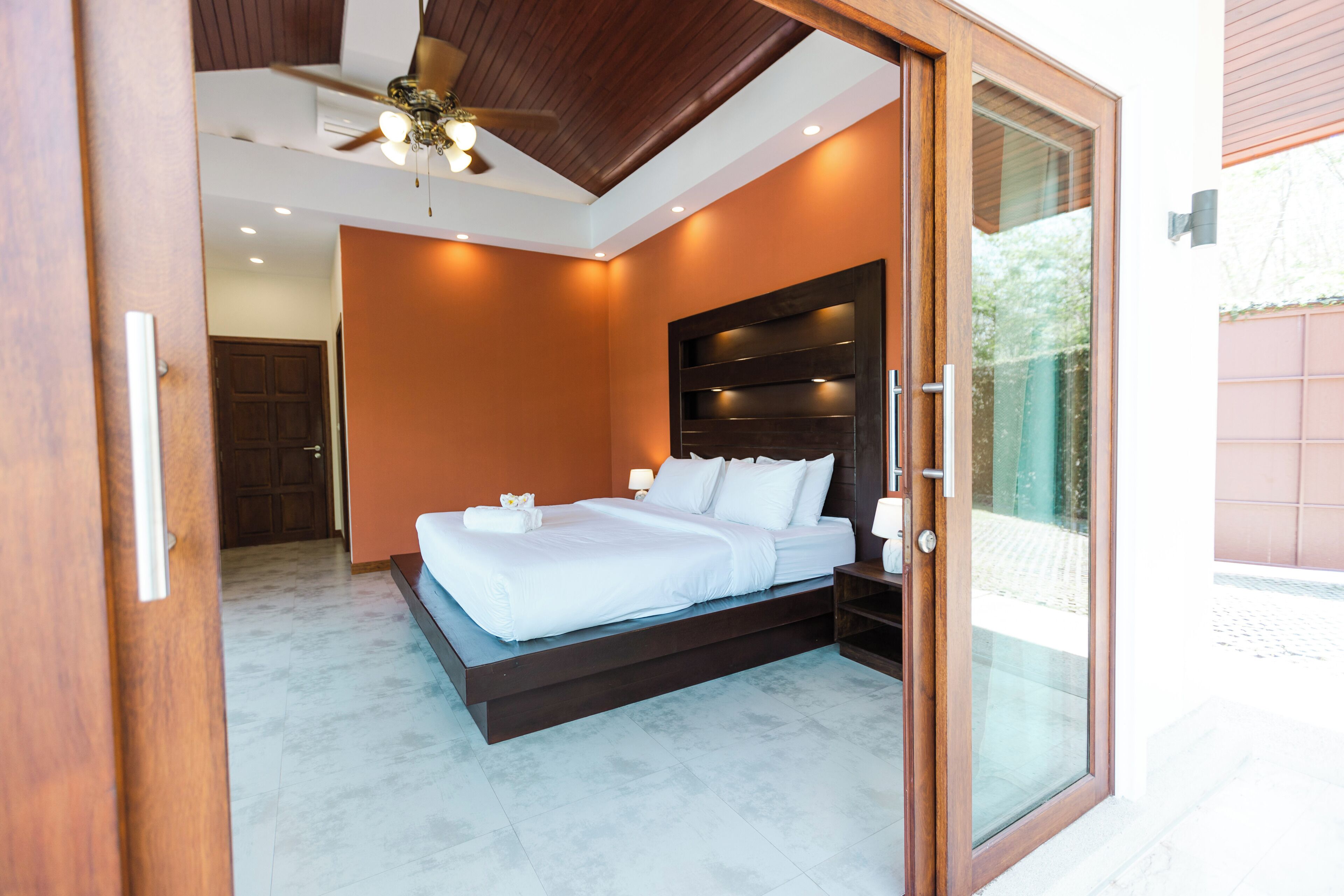 Un dormitorio moderno con una cama grande, un ventilador de techo y un ventanal que da a un área exterior.