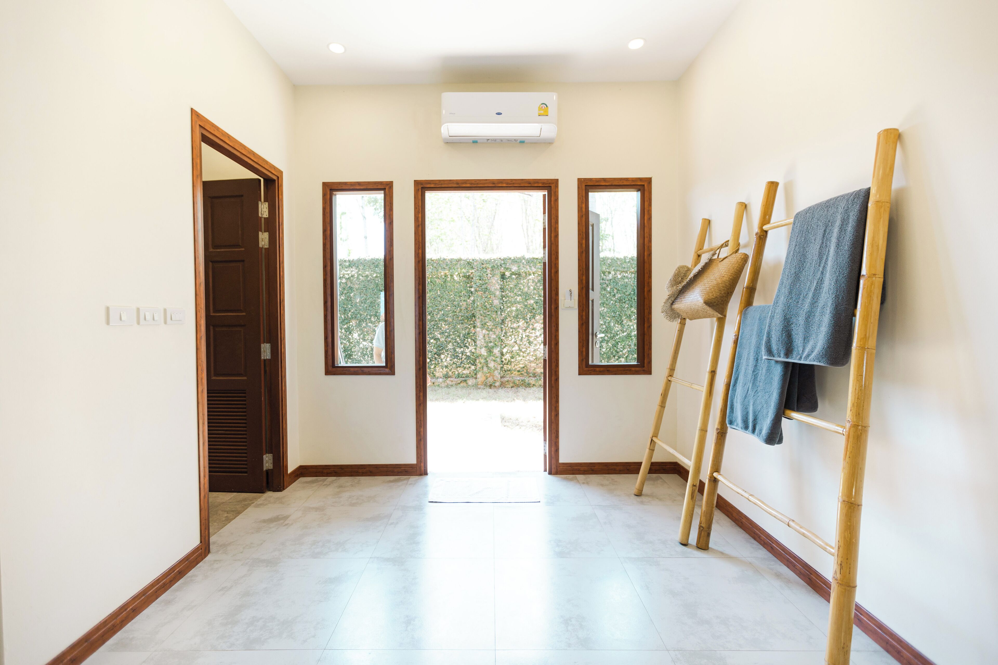 Un couloir avec une porte en bois, une fenêtre et un échafaudage en bambou sur lequel sont posées des serviettes.