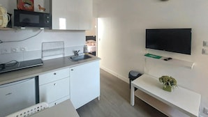 A modern kitchen with a microwave, sink, and white cabinets. There is a small table with a plant and a TV mounted on the wall. - Stunning apartment in Berck plage with WiFi (Berck plage)