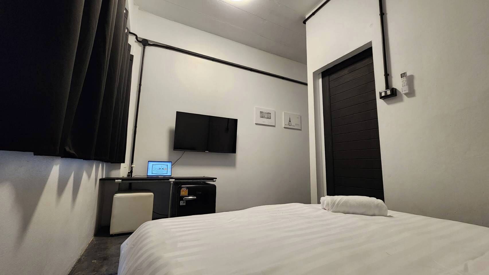 Una camera d'albergo con un letto, una scrivania con un portatile, una televisione e una porta.
