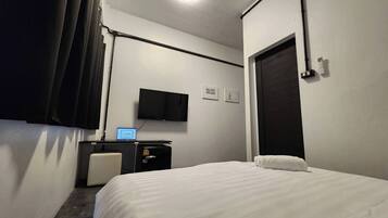 Una camera d'albergo con un letto, una scrivania con un portatile, una televisione e una porta.