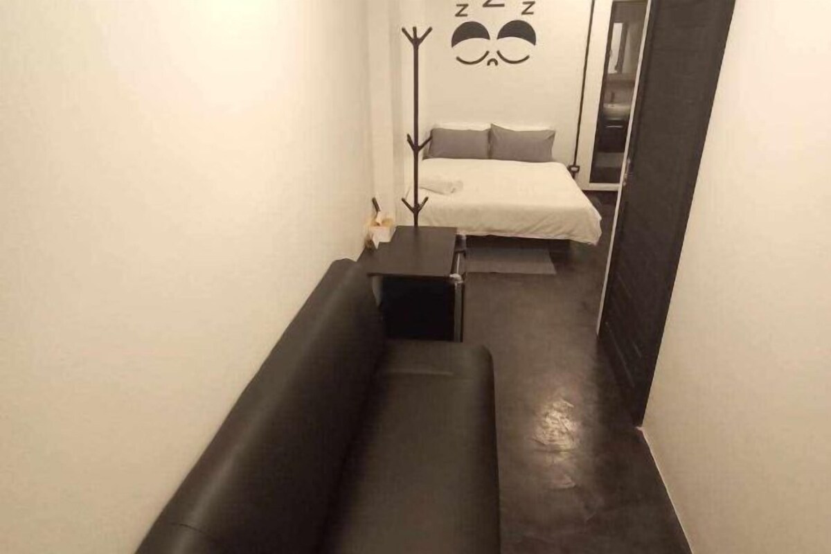 A narrow hallway with a black bench, a bed with white bedding, and a wall with a 'Zzz' decoration.