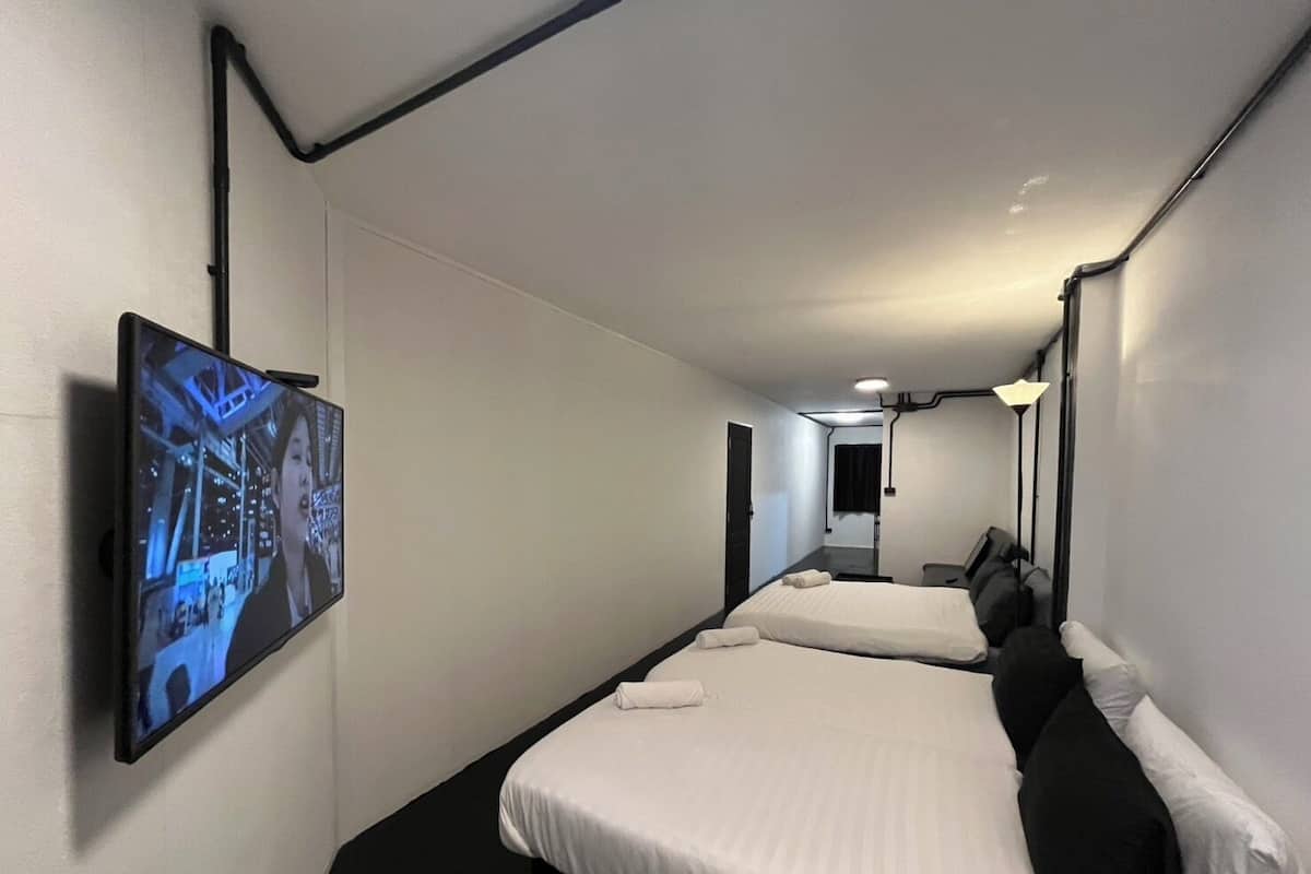 A hotel room with two beds, a flat-screen TV mounted on the wall, and a corridor leading to a bathroom.