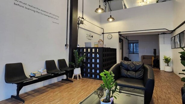 Un espace de bureau moderne avec un long comptoir d’accueil, des chaises noires, une table en verre agrémentée d’objets décoratifs et un canapé en cuir noir.
