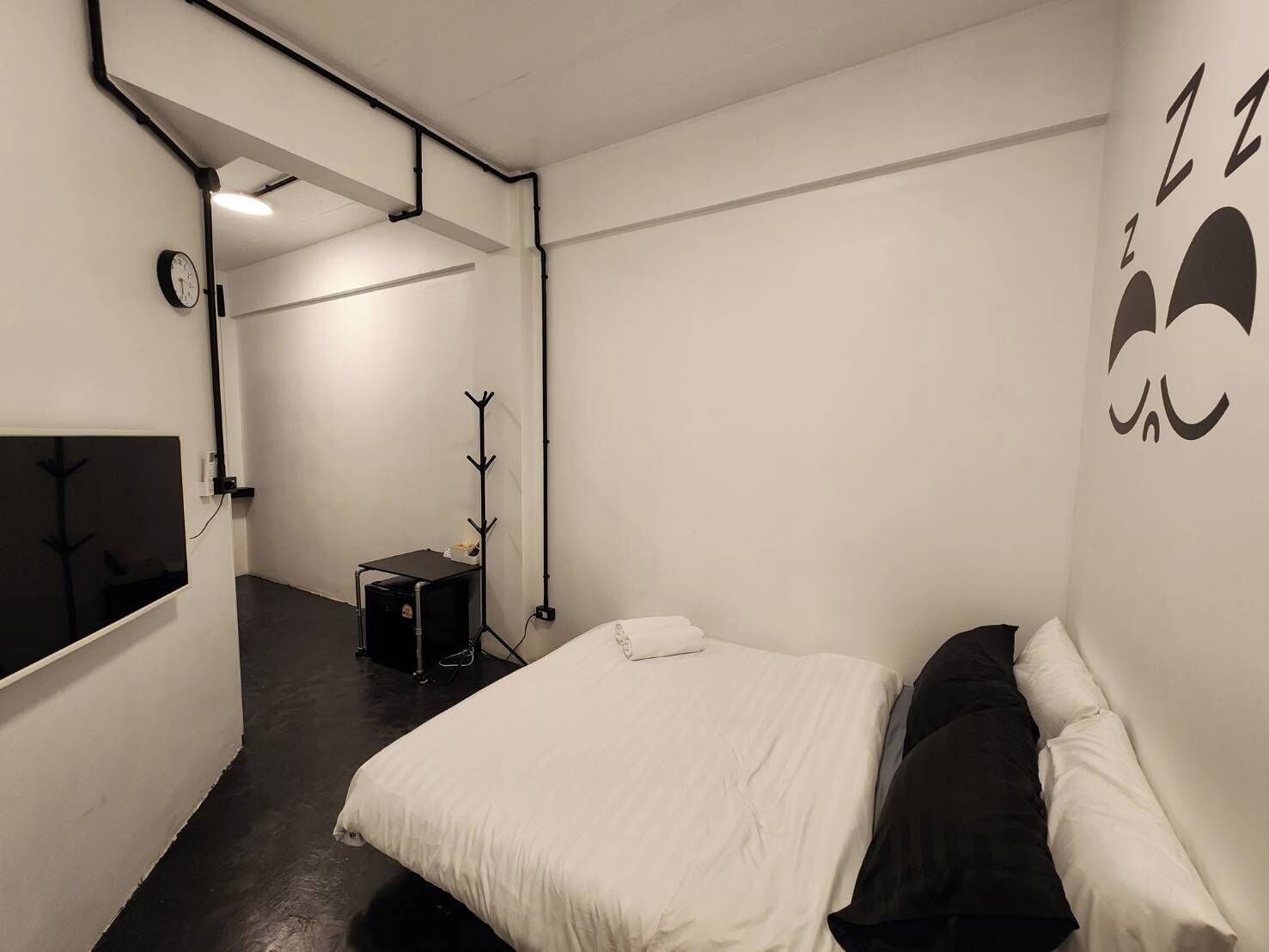 A bedroom with a bed, a coat rack, a small table, and a clock on the wall.
