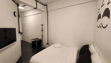 A bedroom with a bed, a coat rack, a small table, and a clock on the wall.