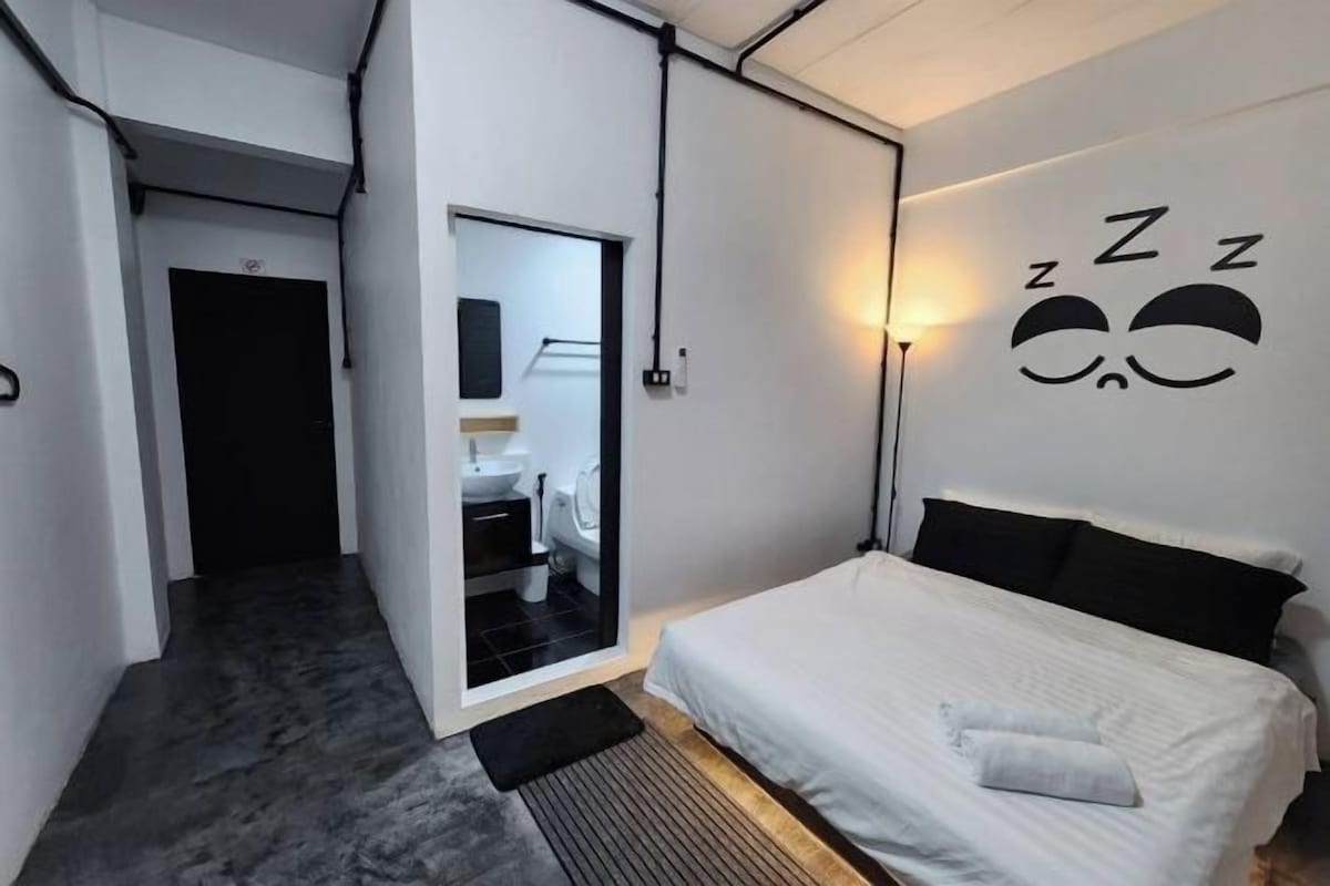 A modern bedroom with a bed, a wall-mounted light, and a mirror reflecting a bathroom.