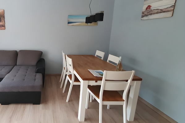 A room with a sofa, a wooden dining table with chairs, and artwork on the walls.