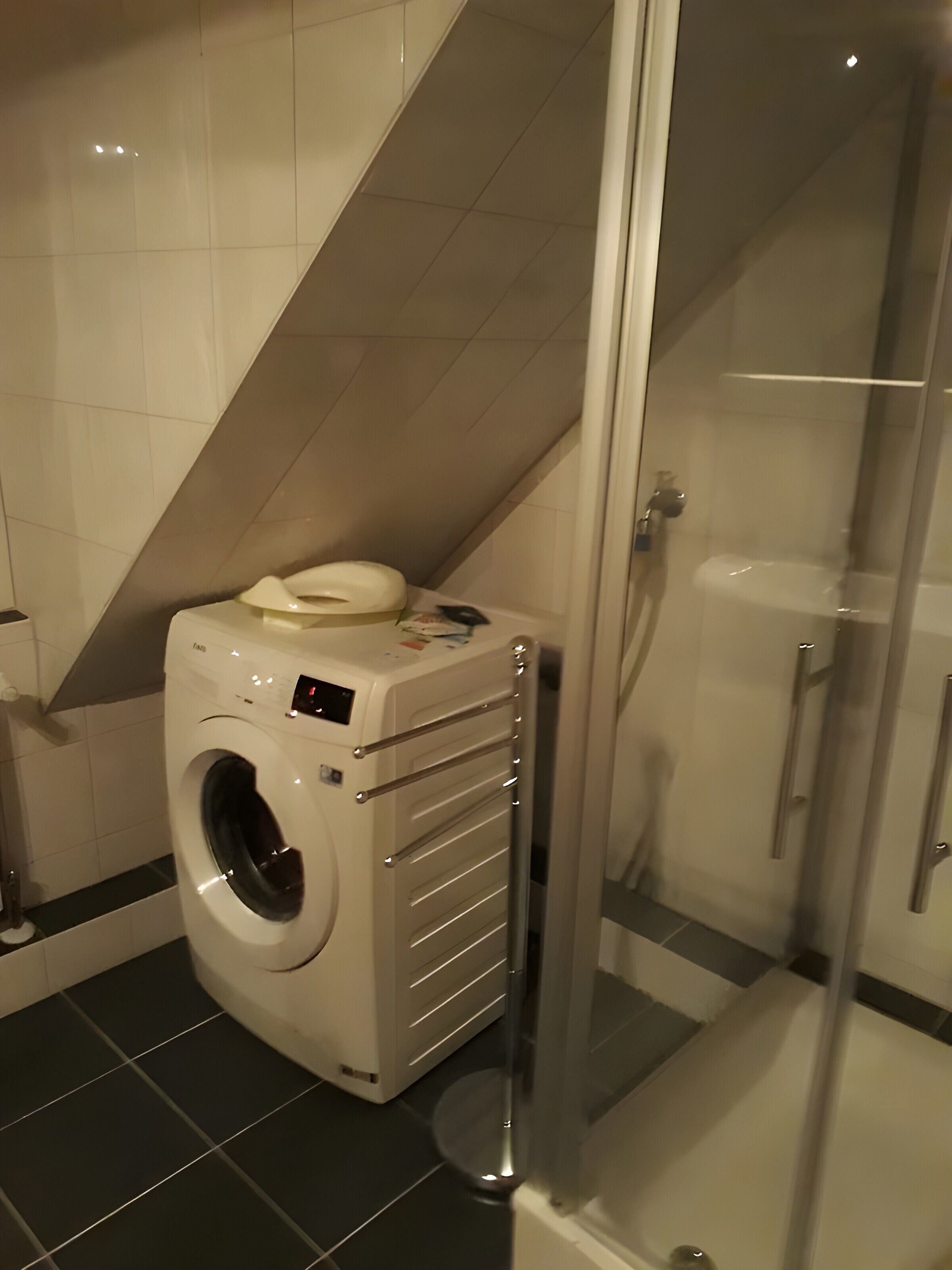 A compact bathroom with a washing machine, a glass shower enclosure, and a tiled floor.