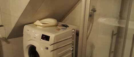 A compact bathroom with a washing machine, a glass shower enclosure, and a tiled floor.