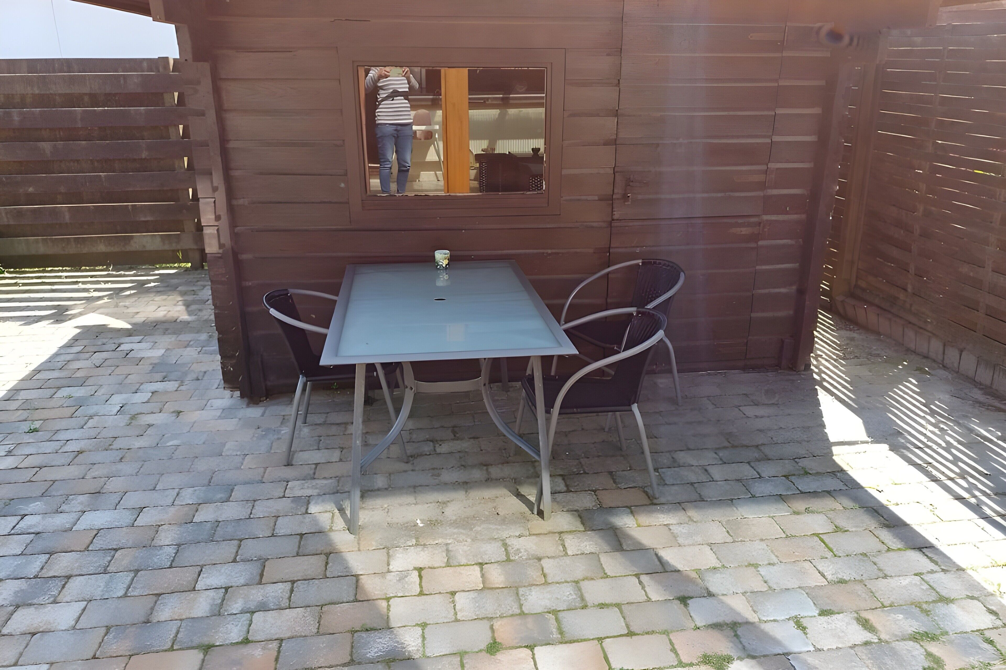 A patio with a table and chairs, a wooden fence, and a window.