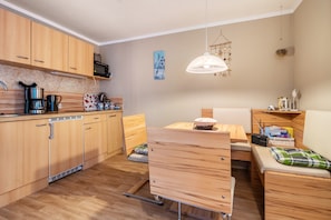 Une cuisine compacte avec des meubles en bois, un lave-vaisselle, une machine à café et un four à micro-ondes. On y trouve également un coin repas avec un banc et un luminaire suspendu.