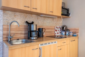 Una cocina con armarios de madera, un lavamanos de acero inoxidable, una cafetera, un tostador y un microondas.