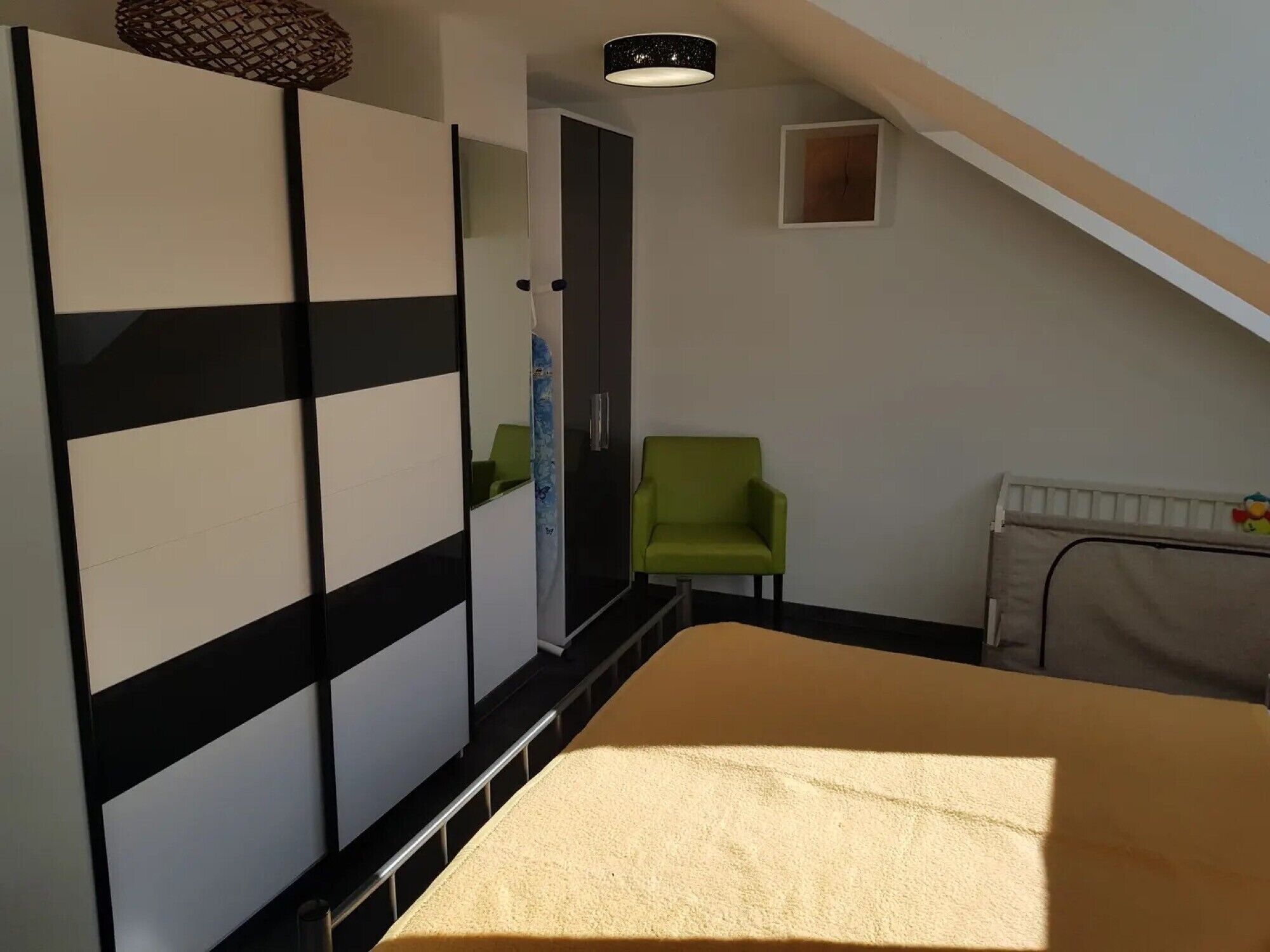 A bedroom with a bed, a green chair, a wardrobe, and a small window.