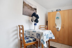 Zona pranzo con tavolo ricoperto da una tovaglia a tema nautico, una sedia di legno con cuscino a quadri, un vaso con fiori e un armadio in legno con specchio.