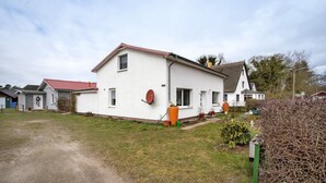 Ett vitt hus i två våningar med ett rött tak, en satellitparabol och en trädgård med krukväxter.