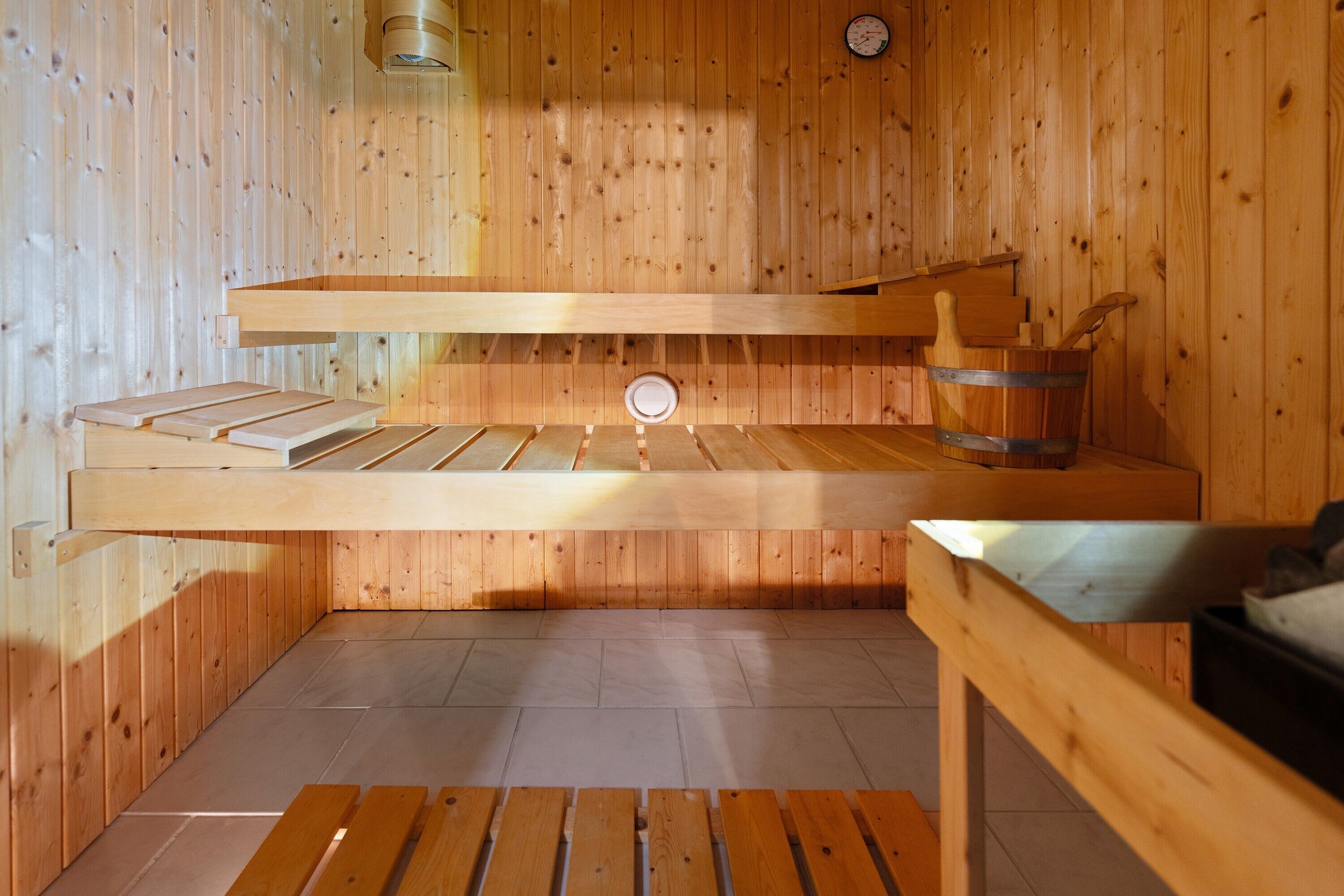 Una sauna de madera con bancos, un cubo y un calentador fijado a la pared.
