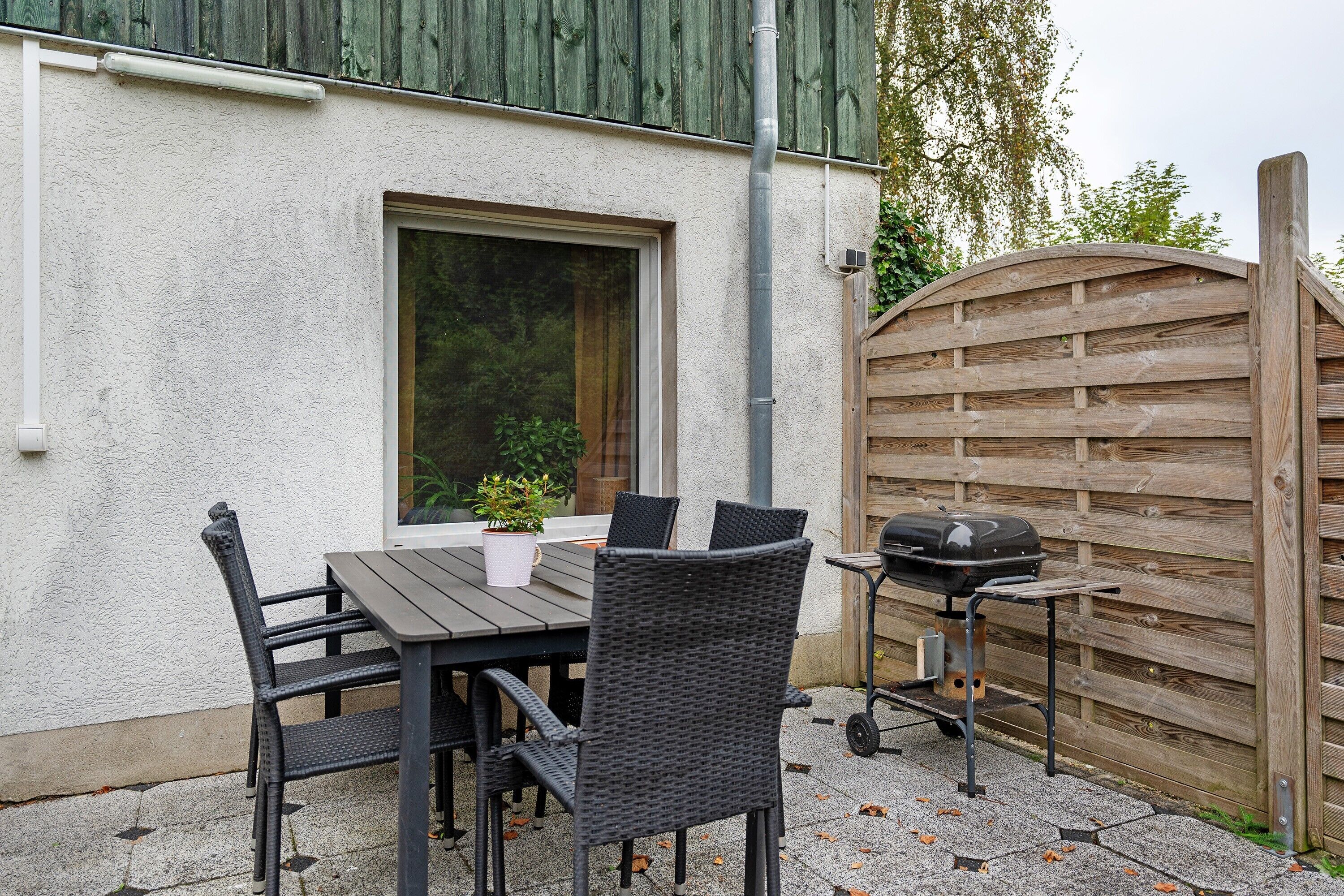 Una veranda esterna con tavolo e sedie, un barbecue e un recinto in legno.