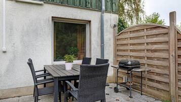 Una veranda esterna con tavolo e sedie, un barbecue e un recinto in legno.
