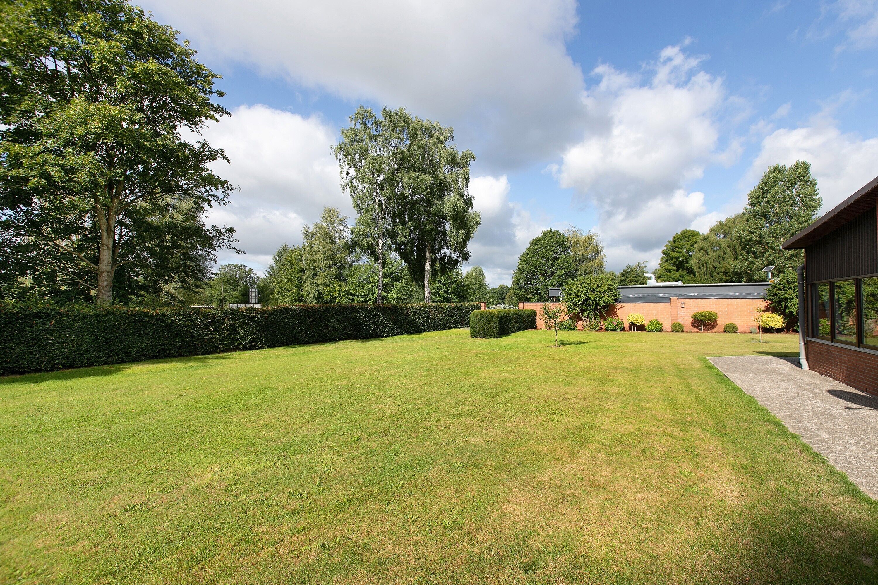 A well-maintained lawn with a brick building and a hedge in the background.