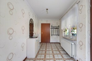 Un pasillo con papel tapiz estampado, una puerta de madera, un radiador y un perchero colgado.