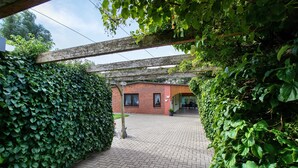 A brick building with a covered patio area, surrounded by dense green foliage. - Apartment 'Ferienwohnung Sawade' with Private Terrace, Shared Garden and Wi-Fi (Schafstedt)