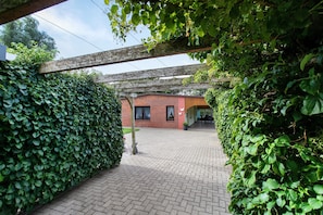 A brick building with a covered patio area, surrounded by dense green foliage. - Apartment 'Ferienwohnung Sawade' with Private Terrace, Shared Garden and Wi-Fi (Schafstedt)