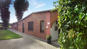 A brick building with a paved walkway, a wooden fence, and lush greenery. - Apartment 'Ferienwohnung Sawade' with Private Terrace, Shared Garden and Wi-Fi (Schafstedt)