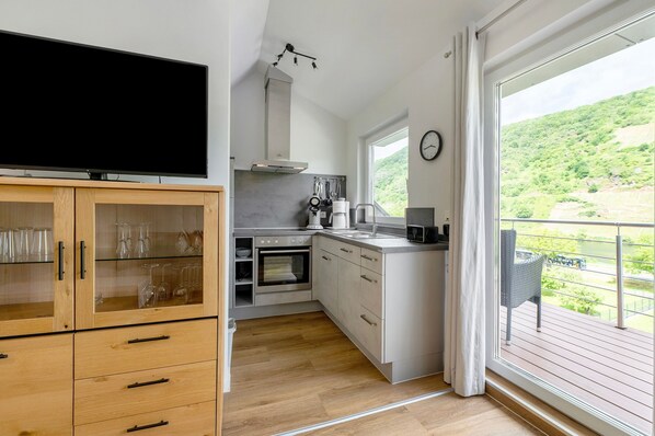 Eine moderne Küche mit Flachbildfernseher, Holzschränken, Backofen, Mikrowelle und einem großen Fenster mit Blick auf Grünflächen.