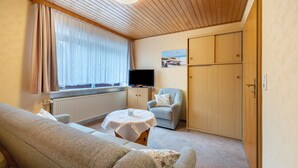 A cozy room with a sofa, a chair, a small table with a cup, a television, and a wardrobe. - Apartment 'Haus Stoldt, Wohnung 2' with Shared Terrace, Shared Garden and Wi-Fi (Meldorf)