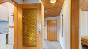 A hallway with a wooden door, a kitchen area, and a bed. - Apartment 'Haus Stoldt, Wohnung 2' with Shared Terrace, Shared Garden and Wi-Fi (Meldorf)