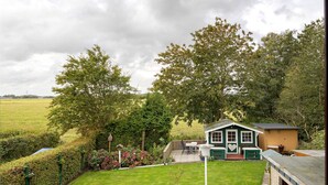 A house with a green exterior, a deck with outdoor furniture, and a garden with a lawn and hedges. - Apartment 'Haus Stoldt, Wohnung 2' with Shared Terrace, Shared Garden and Wi-Fi (Meldorf)