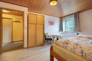 A bedroom with a wooden ceiling, a bed with floral bedding, a chair, a desk, and a window with curtains. - Apartment 'Haus Stoldt, Wohnung 1' with Shared Terrace, Shared Garden and Wi-Fi (Meldorf)