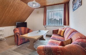 A loft-style room with a wooden ceiling, a sofa, a chair, a table, and a window with curtains. - Apartment 'Haus Stoldt, Wohnung 1' with Shared Terrace, Shared Garden and Wi-Fi (Meldorf)