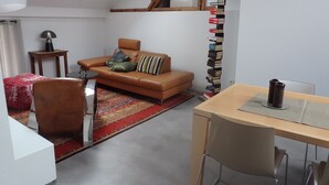 A modern living room with a brown leather sofa, a small round table, a wooden desk, and a bookshelf. - Apartment 'Fewoimdorf' with Wi-Fi (Wertheim)