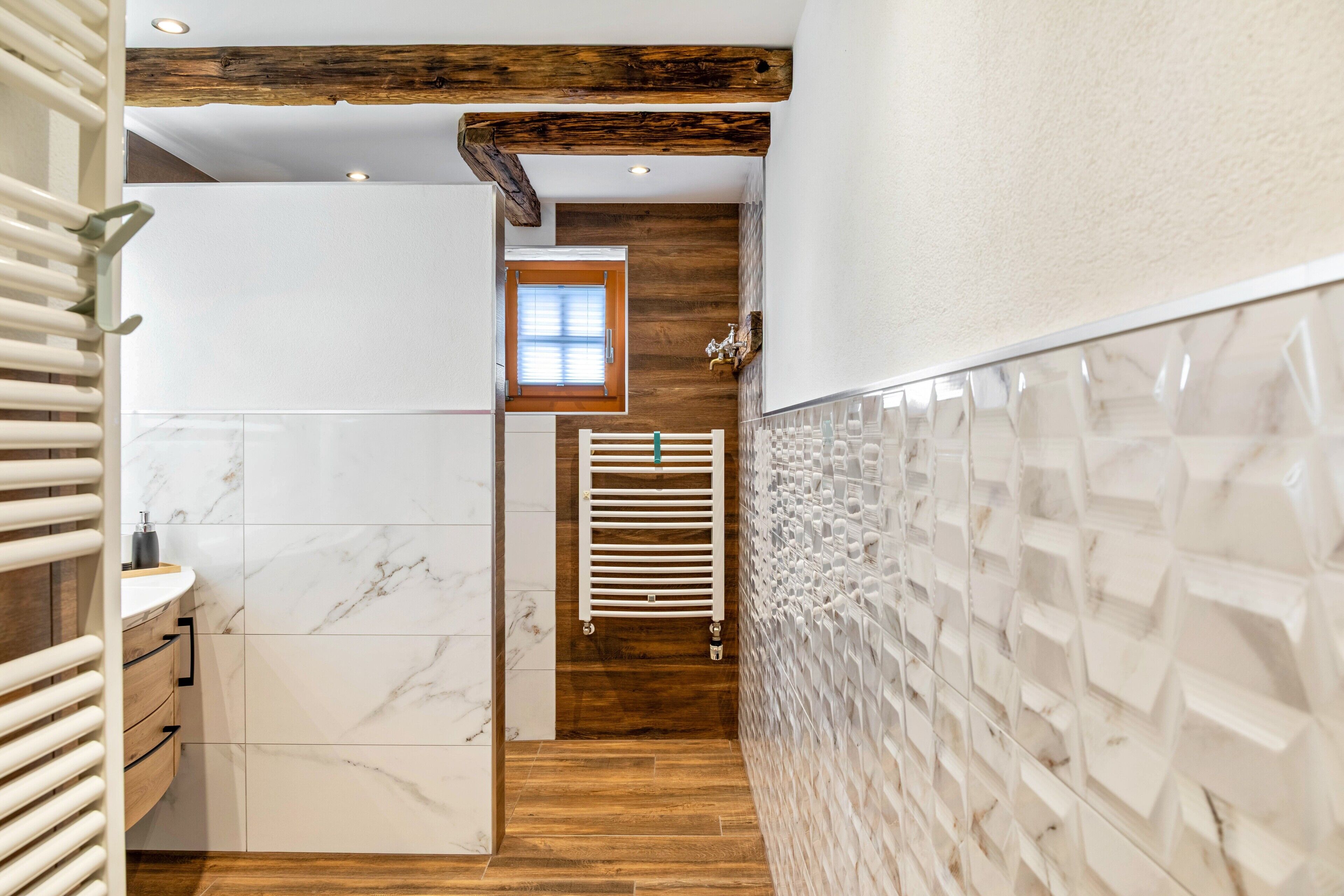 Un pasillo estrecho con suelo de madera, paredes de baldosas blancas y una viga de techo de madera.