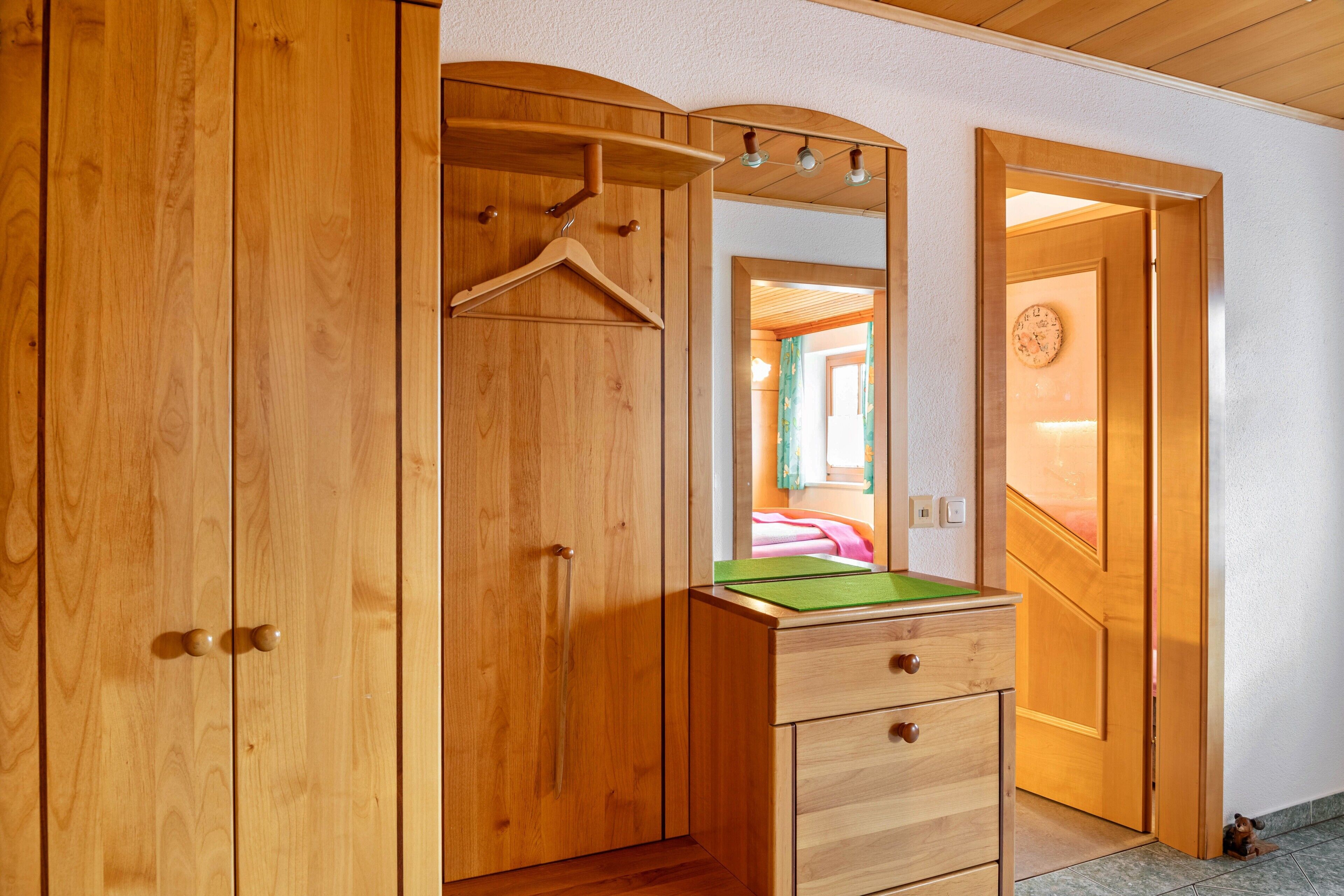 Une armoire en bois avec un miroir, un tapis vert et un porte-vêtements.