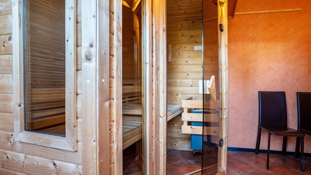 Interior de una cabaña de madera con un vidrio que da a una zona de descanso, un pequeño mueble azul para guardar cosas y dos sillas.