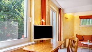 Una habitación con escritorio de madera, una silla, televisor, sofá y ventana con cortinas.