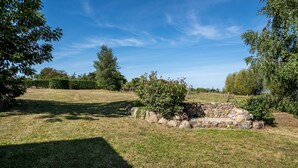 Un área verde al aire libre con una estructura de piedra, árboles y un cielo azul despejado.